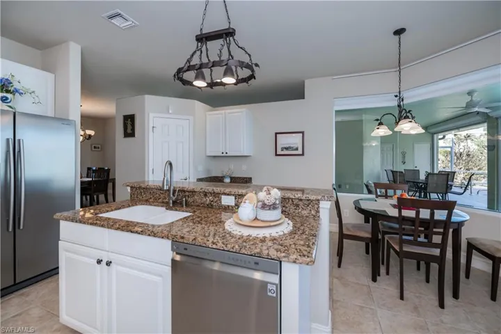 Kitchen featuring a chandelier, appliances with stainless steel finishes, a center island with sink, hanging light fixtures, and dark stone counters
