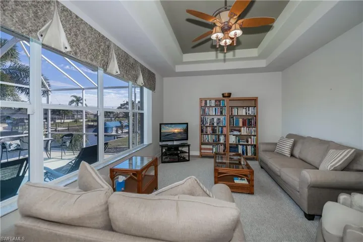 Living area with carpet floors, a raised ceiling, a sunroom, and a ceiling fan