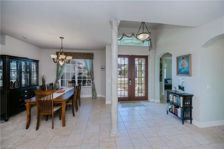 Dining space with light tile patterned floors, decorative columns, french doors, and a chandelier