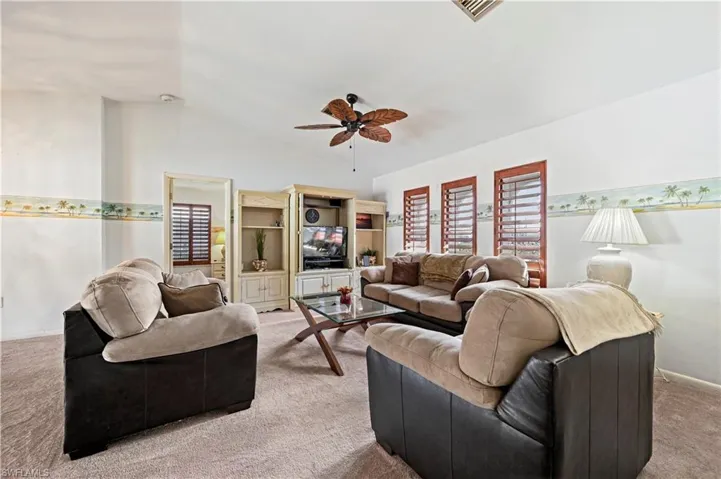 Living room featuring vaulted ceiling, light colored carpet, and ceiling fan