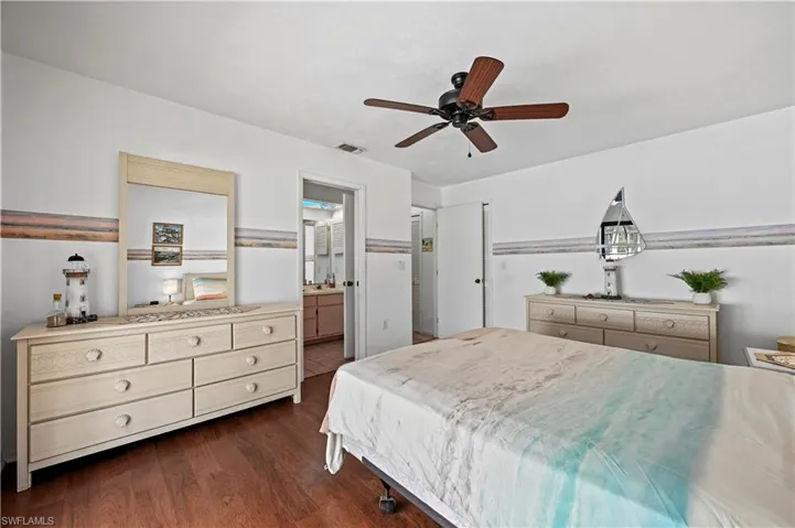 Bedroom with dark hardwood / wood-style floors, ceiling fan, and ensuite bath