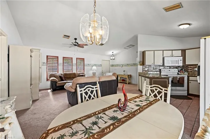 Carpeted dining space featuring vaulted ceiling and ceiling fan with notable chandelier