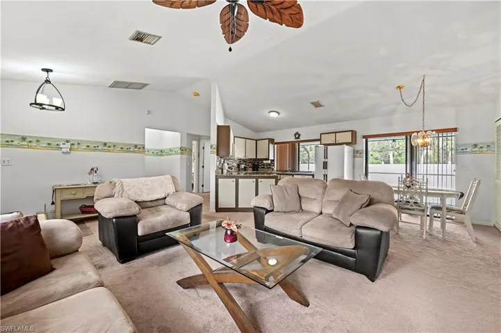 Living room with light colored carpet, lofted ceiling, and ceiling fan with notable chandelier