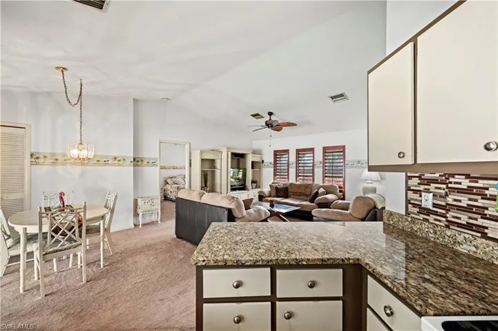 Kitchen featuring white cabinetry, vaulted ceiling, light carpet, ceiling fan with notable chandelier, and backsplash
