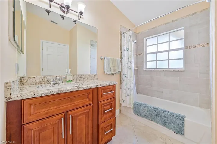 Bathroom featuring vanity, vaulted ceiling, shower / bath combo with shower curtain, and tile patterned flooring