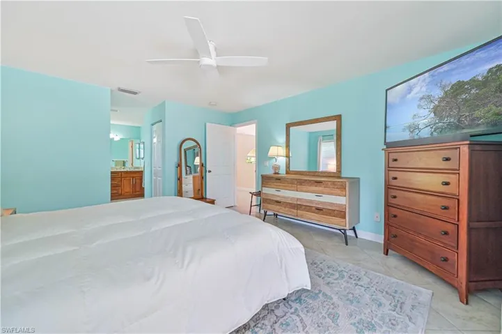 Bedroom with light tile patterned flooring, ceiling fan, and ensuite bath
