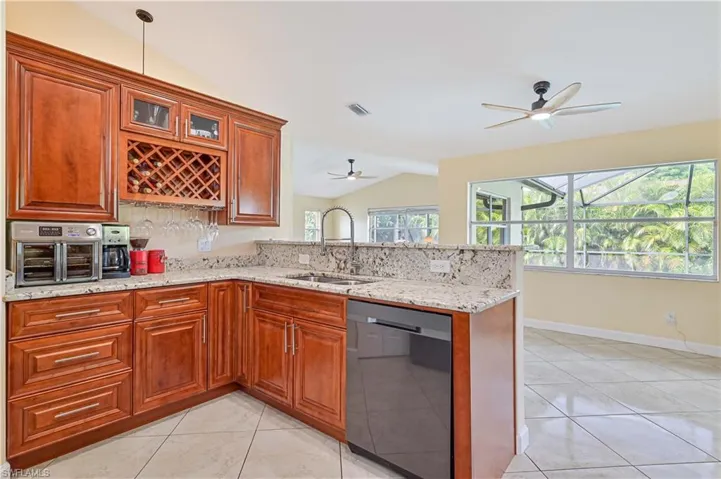 Kitchen featuring lofted ceiling, light tile patterned floors, light stone countertops, dishwasher, and sink