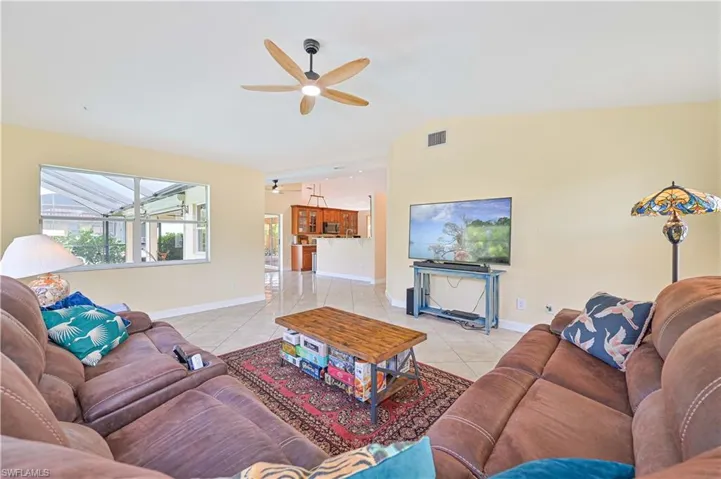 Living room featuring vaulted ceiling, ceiling fan, and light tile patterned flooring