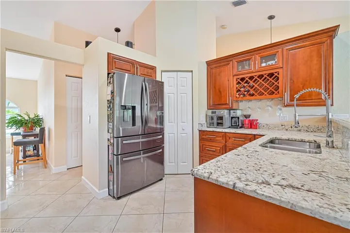 Kitchen featuring light tile patterned floors, stainless steel fridge with ice dispenser, light stone countertops, vaulted ceiling, and sink