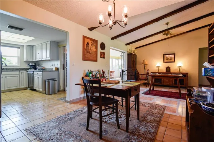 Tiled dining area with a notable chandelier, lofted ceiling with beams, and a textured ceiling