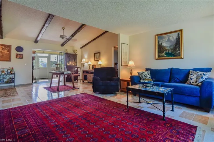 Living room featuring tile floors, lofted ceiling with beams, and a textured ceiling