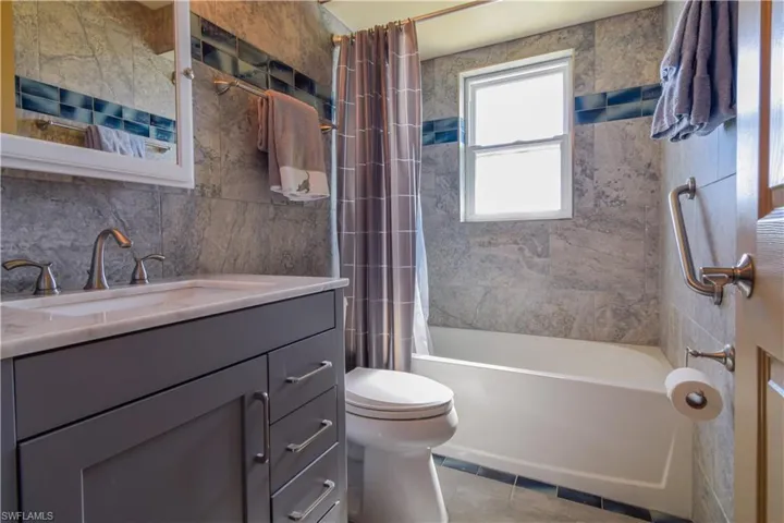 Full bathroom with tile walls, oversized vanity, toilet, tile flooring, and shower / bath combo with shower curtain