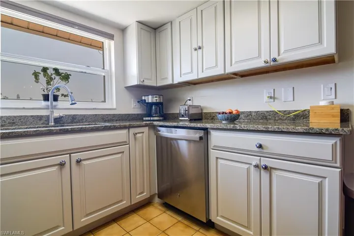 Kitchen featuring dark stone countertops, sink, stainless steel dishwasher, and light tile flooring