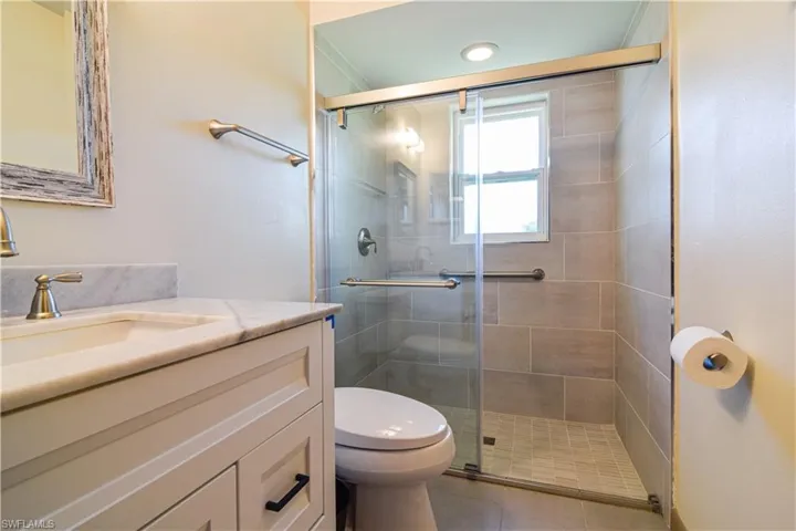 Bathroom featuring a shower with shower door, vanity, toilet, and tile floors