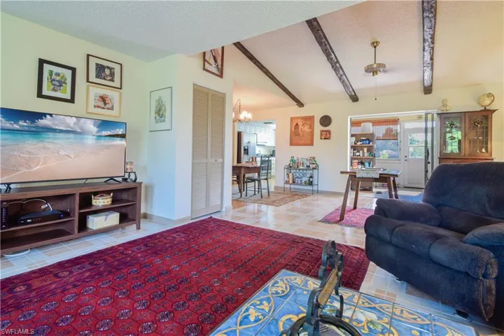 Living room featuring tile flooring, vaulted ceiling with beams, a textured ceiling, and a chandelier