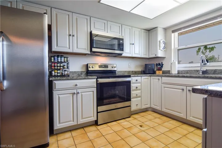 Kitchen featuring white cabinets, stainless steel appliances, dark stone countertops, sink, and light tile floors