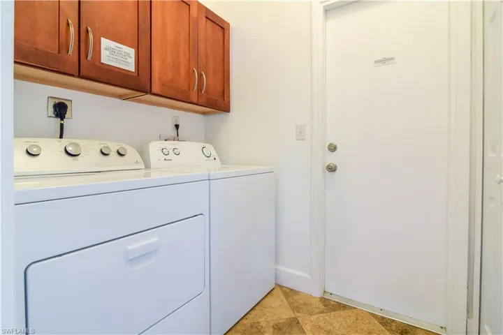 Clothes washing area featuring washing machine and clothes dryer, hookup for an electric dryer, cabinets, and light tile floors