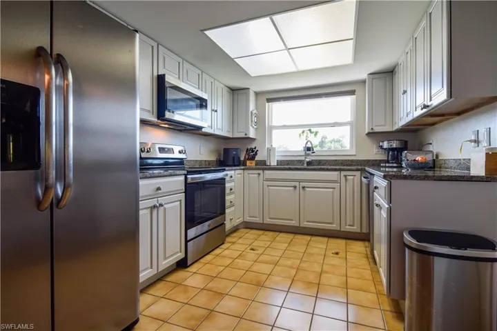 Kitchen with sink, dark stone countertops, light tile floors, and stainless steel appliances