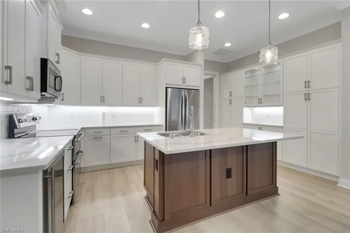 Kitchen with light wood-type flooring, backsplash, white cabinets, and appliances with stainless steel finishes