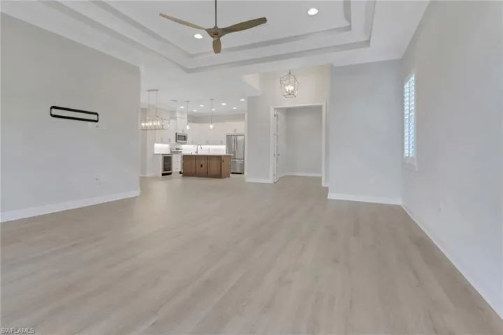 Unfurnished living room with a raised ceiling, ceiling fan with notable chandelier, baseboards, and light wood-style flooring