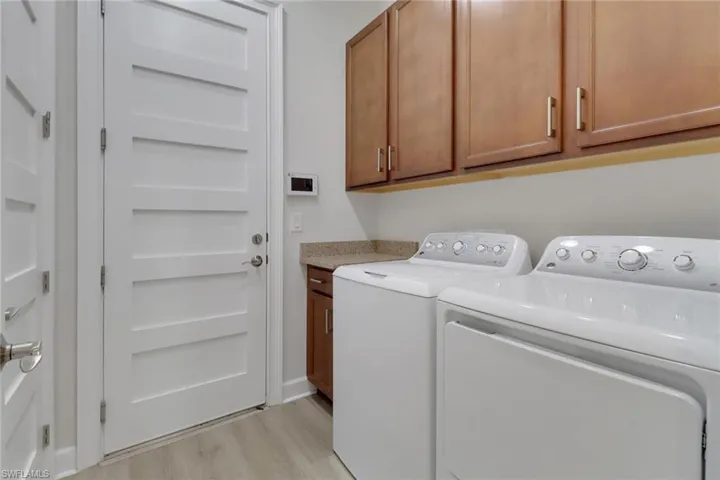 Clothes washing area featuring washing machine and dryer, cabinet space, and light wood-type flooring