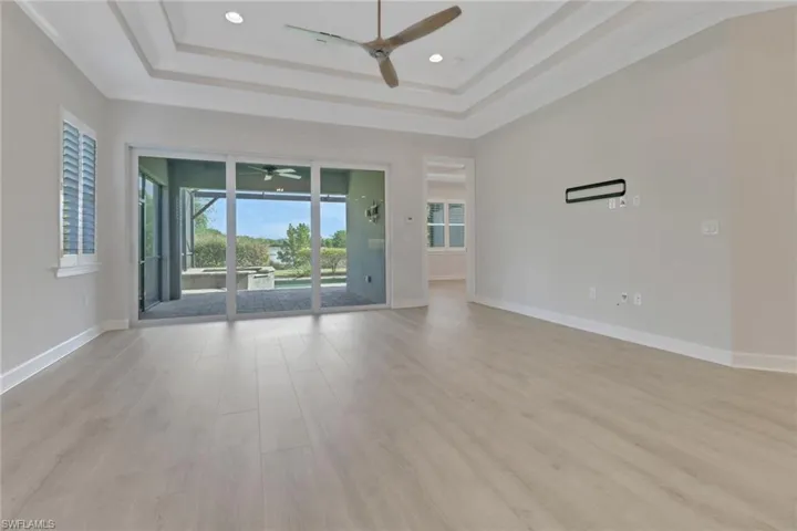 Unfurnished living room featuring baseboards, light wood-style floors, a tray ceiling, and ceiling fan