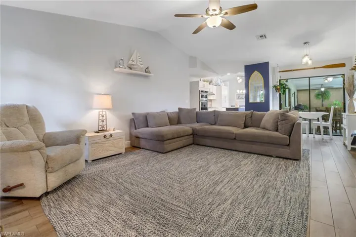 Living room with ceiling fan, light hardwood / wood-style flooring, and lofted ceiling