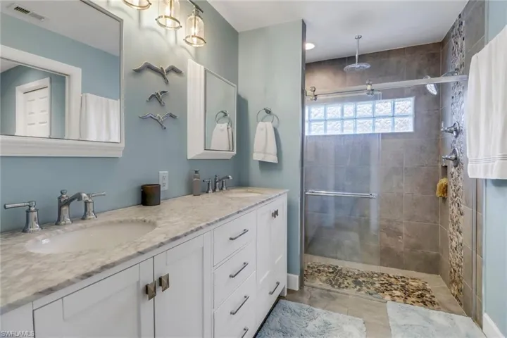 Bathroom featuring double sink vanity, a tile shower, and tile patterned flooring
