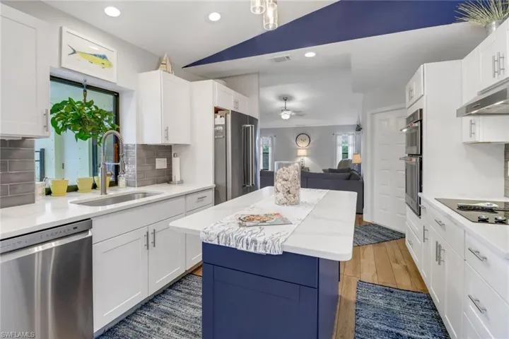 Kitchen featuring a kitchen island, backsplash, stainless steel appliances, sink, and wood-type flooring