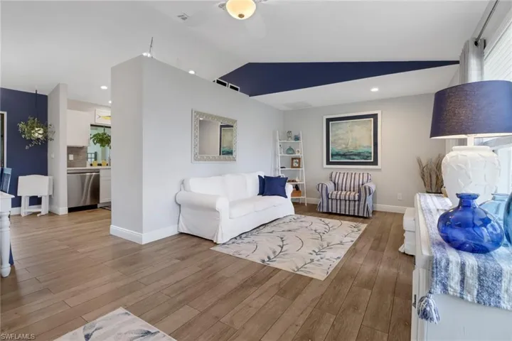 Living room with ceiling fan, light wood-type flooring, and vaulted ceiling