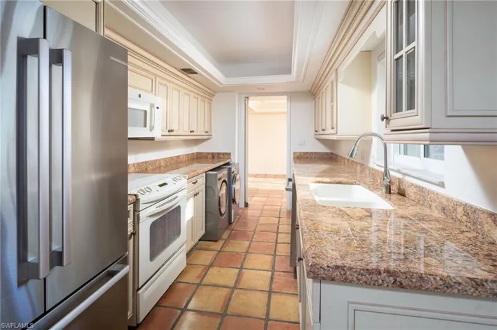 Kitchen featuring natural stone countertops, custom cream cabinetry, stainless steel refrigerator, white dual-basin sink with arched faucet, and tiled flooring