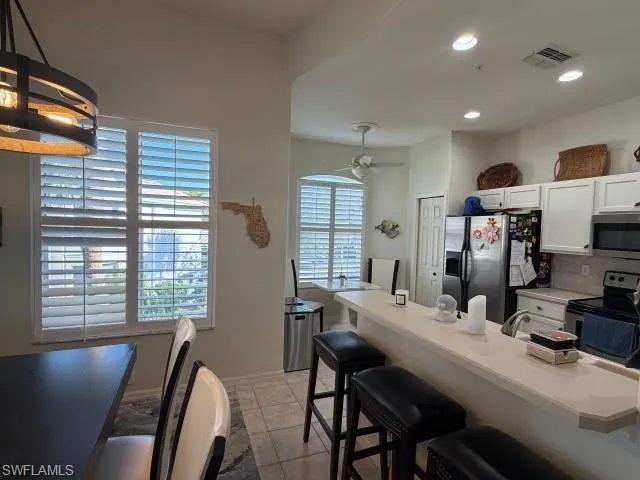 Kitchen featuring a kitchen bar, stainless steel appliances, white cabinets, tasteful backsplash, and light countertops
