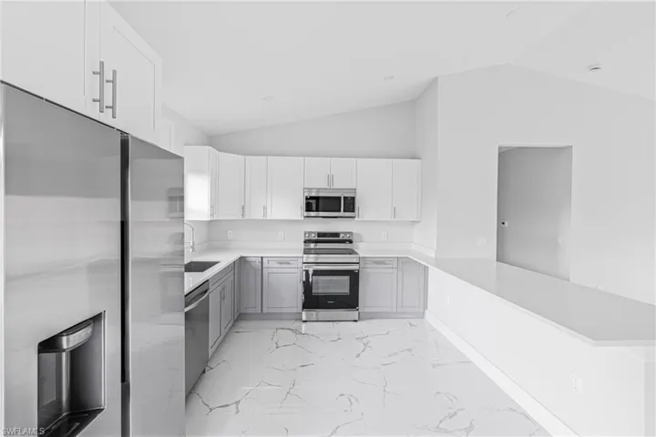 Kitchen featuring stainless steel appliances, light marble finish flooring, white cabinets, a peninsula, and light stone counters
