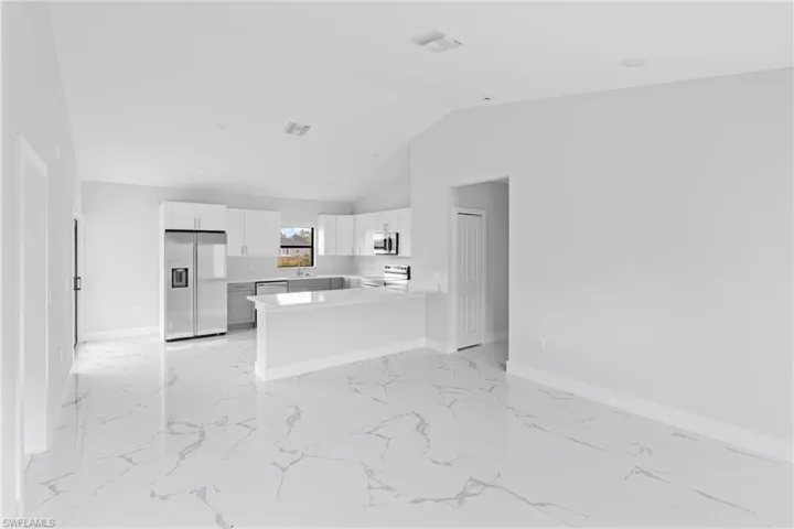 Kitchen with stainless steel appliances, a peninsula, white cabinets, light marble finish floors, and lofted ceiling