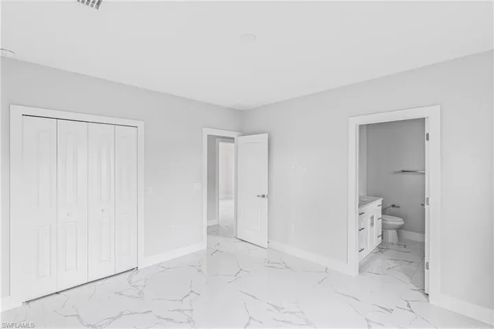 Unfurnished bedroom featuring light marble finish flooring, a closet, and ensuite bathroom