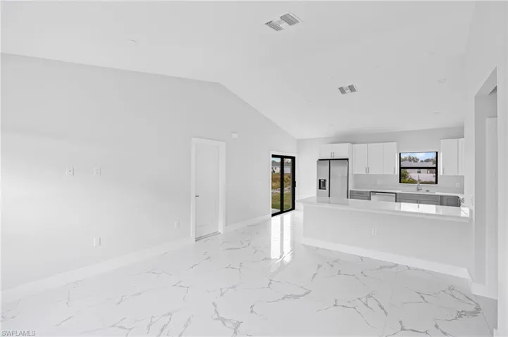Unfurnished living room with vaulted ceiling and light marble finish flooring