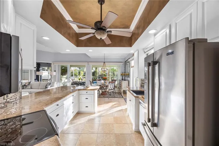 Kitchen with high end refrigerator, a tray ceiling, white cabinets, a peninsula, and recessed lighting