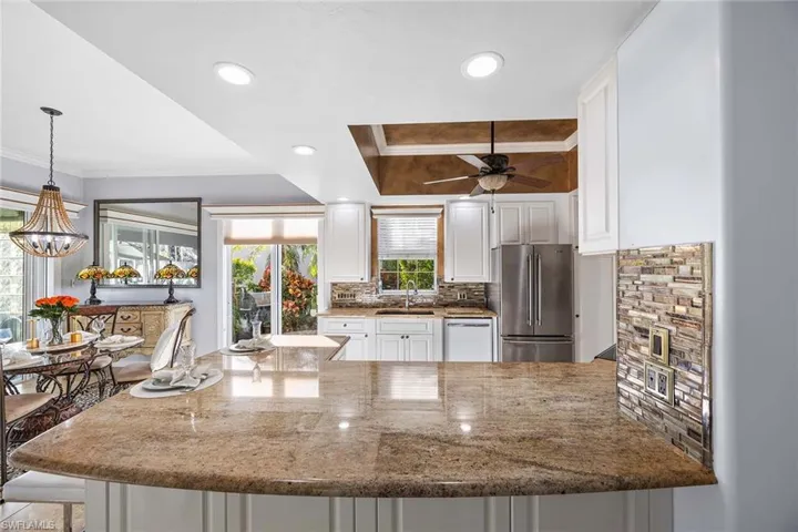 Kitchen with a peninsula, light stone counters, decorative backsplash, ornamental molding, and white cabinets