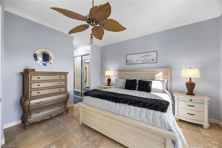 Bedroom with crown molding, a closet, a ceiling fan, and stone tile floors