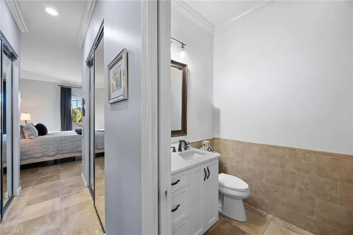 Half bath with crown molding, vanity, wainscoting, tile walls, and connected bathroom