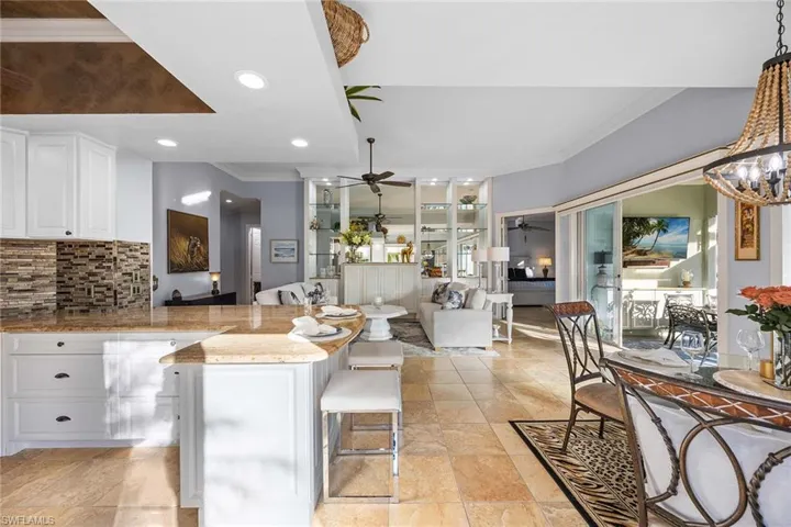 Kitchen featuring crown molding, white cabinets, light stone counters, decorative backsplash, and a kitchen bar