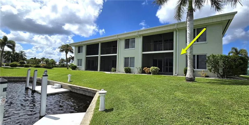 Multi-story exterior featuring a screened-in ground-level lanai, manicured lawn, and dedicated canal-front boat dockage
