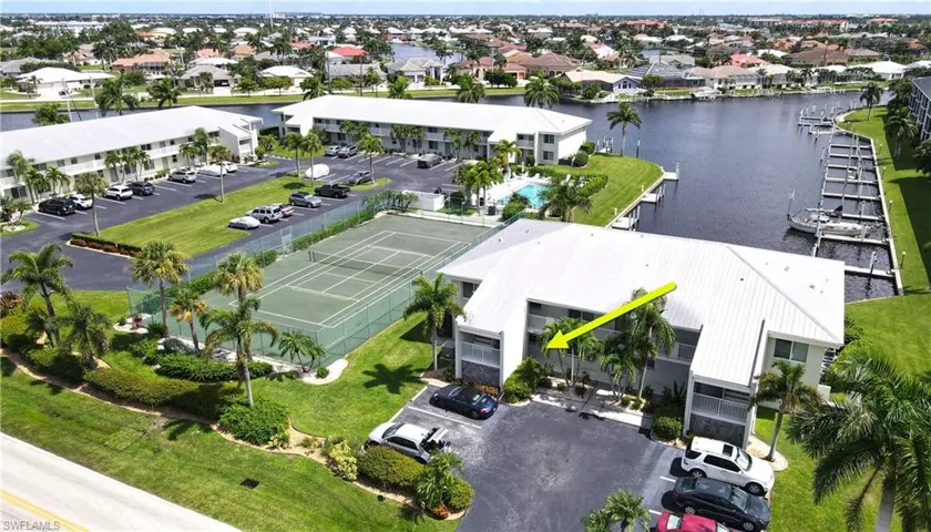 Aerial perspective of a multi-unit property featuring a waterfront canal position, boat slips, a tennis court, and a swimming pool