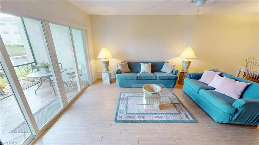 Open-concept interior featuring wood-finish tile flooring, a white ceiling fan, and large sliding glass doors providing outdoor access to a screened lanai with tile surfacing