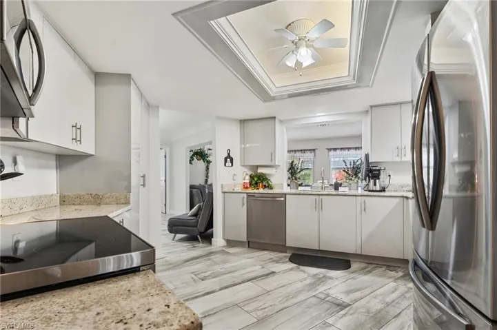 Kitchen with stainless steel appliances, light stone counters, ceiling fan, ornamental molding, and white cabinets