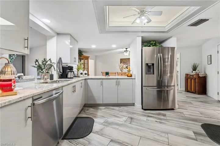 Kitchen featuring stainless steel appliances, light stone counters, ornamental molding, a ceiling fan, and a peninsula
