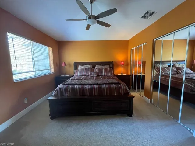 Carpeted master bedroom featuring ceiling fan and multiple closets