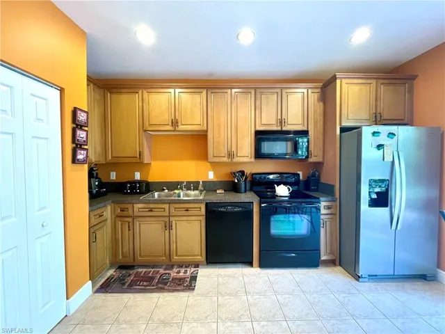 Kitchen with dark countertops, light tile patterned floors, black appliances, and a sink