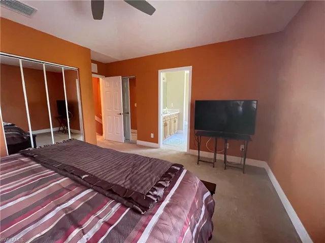 Bedroom with ensuite bathroom, carpet, ceiling fan, and a closet