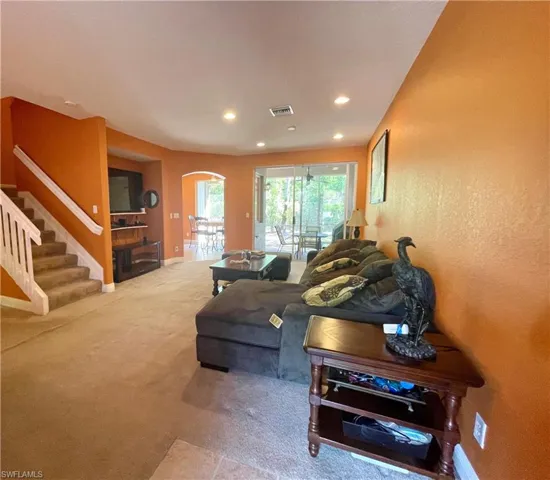 Carpeted living room featuring stairway, visible vents, baseboards, recessed lighting, and arched walkways